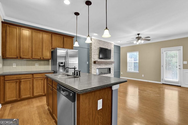 kitchen featuring pendant lighting, crown molding, appliances with stainless steel finishes, a kitchen island with sink, and a fireplace