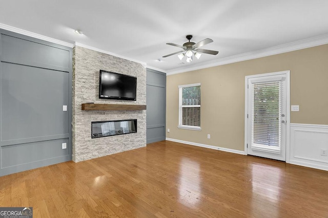 unfurnished living room featuring crown molding, a stone fireplace, hardwood / wood-style floors, and ceiling fan