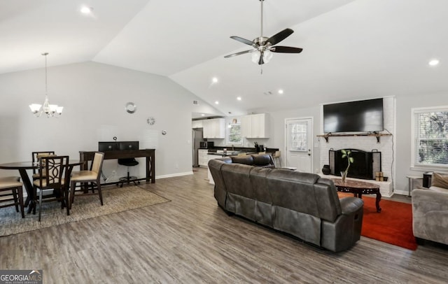 living room with hardwood / wood-style flooring, lofted ceiling, a fireplace, and ceiling fan with notable chandelier