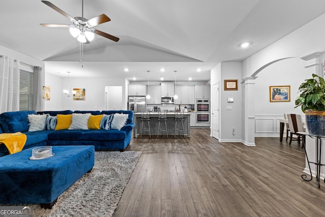 living room featuring dark wood-type flooring, ceiling fan, vaulted ceiling, and decorative columns