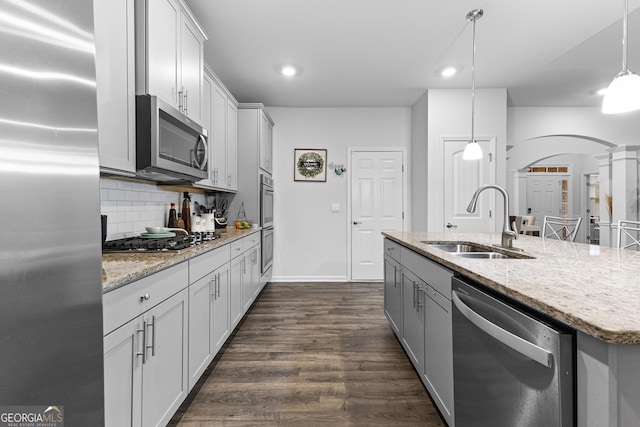 kitchen with appliances with stainless steel finishes, decorative light fixtures, tasteful backsplash, sink, and a kitchen island with sink