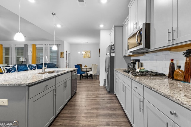 kitchen with pendant lighting, appliances with stainless steel finishes, sink, and an island with sink