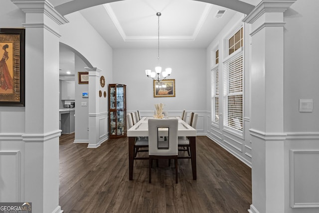 dining area with dark hardwood / wood-style flooring, a notable chandelier, decorative columns, and a raised ceiling