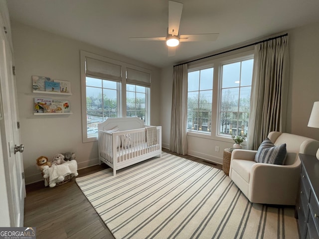 bedroom featuring multiple windows, hardwood / wood-style flooring, a crib, and ceiling fan