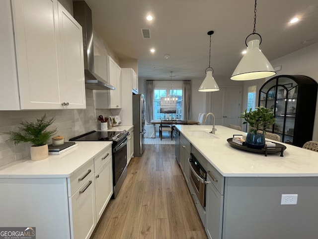 kitchen featuring white cabinetry, hanging light fixtures, stainless steel appliances, and an island with sink