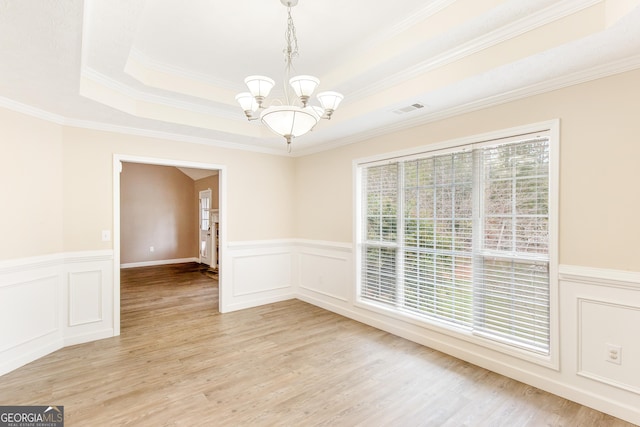 empty room with an inviting chandelier, a tray ceiling, light hardwood / wood-style flooring, and ornamental molding