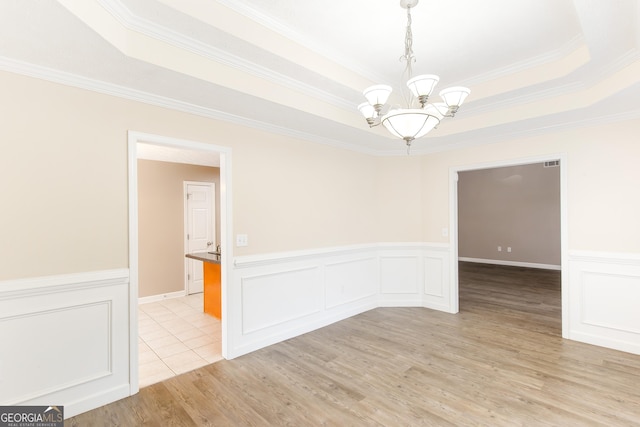 spare room with a tray ceiling, ornamental molding, a chandelier, and light wood-type flooring