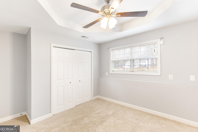 unfurnished bedroom with light carpet, a closet, a raised ceiling, and ceiling fan