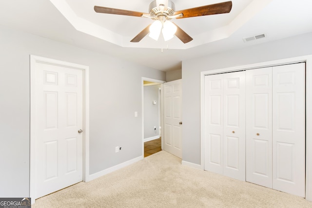 unfurnished bedroom with a raised ceiling, light colored carpet, ceiling fan, and a closet