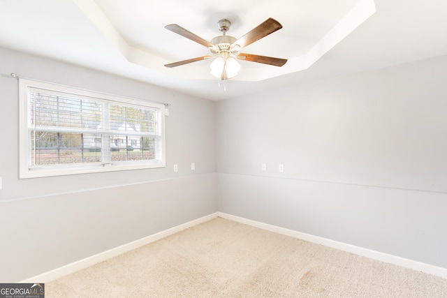 unfurnished room with a raised ceiling, ceiling fan, and carpet flooring