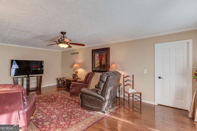 living room with crown molding, ceiling fan, wood-type flooring, and a textured ceiling