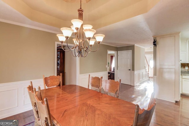 dining area featuring hardwood / wood-style floors, ornamental molding, a raised ceiling, and a chandelier