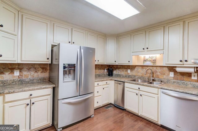 kitchen with cream cabinetry, appliances with stainless steel finishes, sink, and backsplash