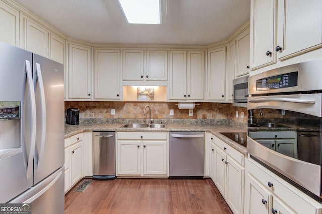 kitchen featuring appliances with stainless steel finishes, tasteful backsplash, sink, light stone counters, and light hardwood / wood-style floors