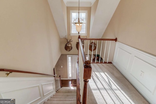 stairway with ornamental molding, carpet, and a notable chandelier