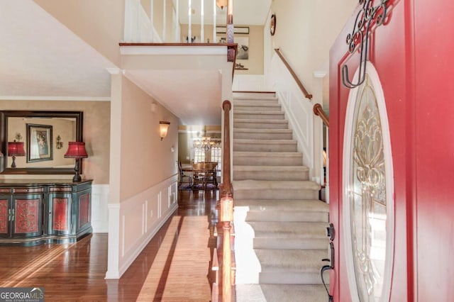 entryway with ornamental molding, wood-type flooring, plenty of natural light, and a towering ceiling