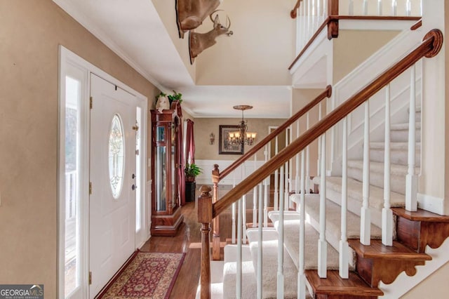 entryway with an inviting chandelier, crown molding, and dark wood-type flooring