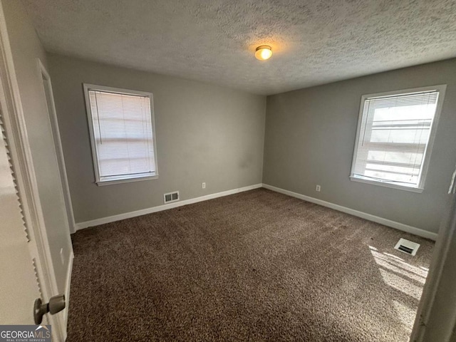 empty room featuring dark carpet and a textured ceiling