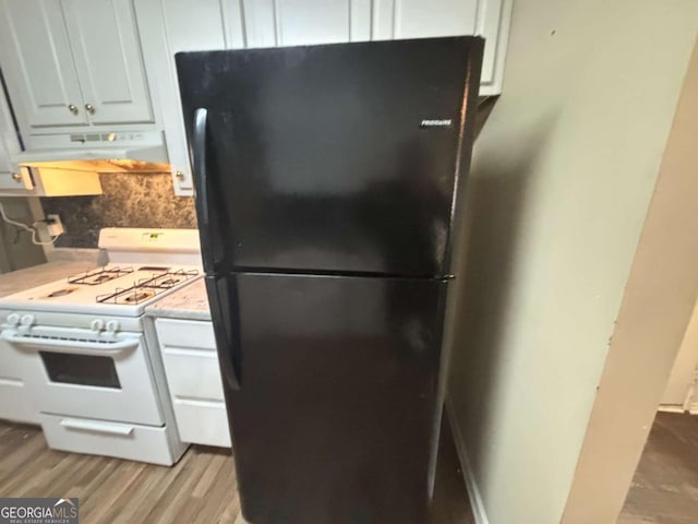 kitchen with light wood-type flooring, black refrigerator, backsplash, white gas range oven, and white cabinets