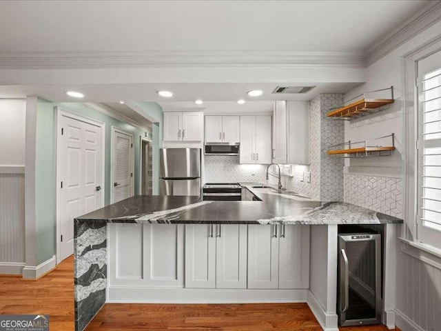 kitchen with appliances with stainless steel finishes, beverage cooler, kitchen peninsula, and white cabinets