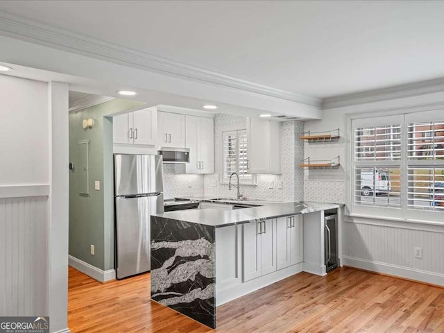 kitchen with appliances with stainless steel finishes, white cabinetry, wine cooler, ornamental molding, and light hardwood / wood-style floors