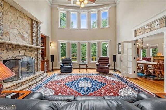 living room with an inviting chandelier, ornamental molding, a stone fireplace, and hardwood / wood-style floors