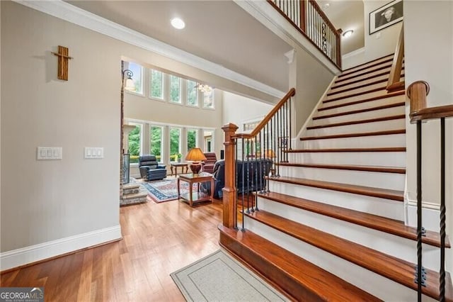 staircase with ornamental molding, hardwood / wood-style floors, and a high ceiling