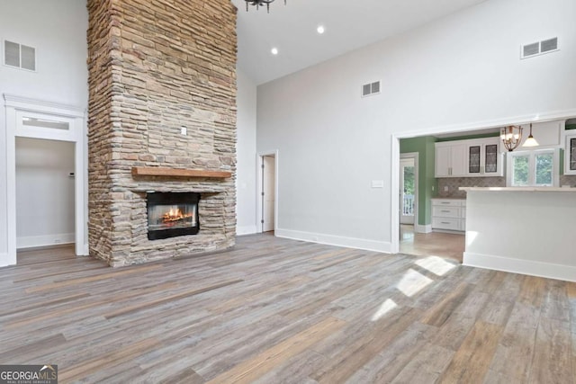 unfurnished living room with an inviting chandelier, a fireplace, light hardwood / wood-style floors, and a high ceiling