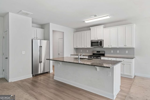 kitchen featuring sink, appliances with stainless steel finishes, white cabinetry, dark stone countertops, and a center island with sink