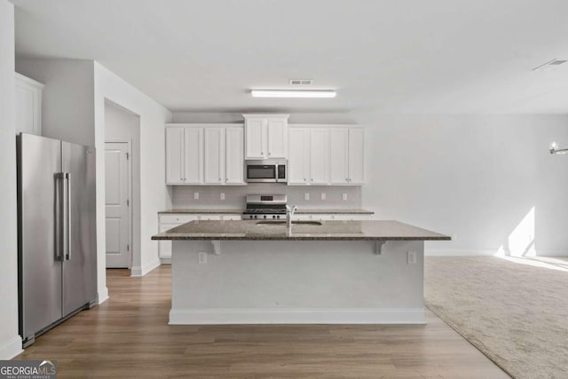 kitchen featuring sink, white cabinetry, dark stone countertops, stainless steel appliances, and an island with sink