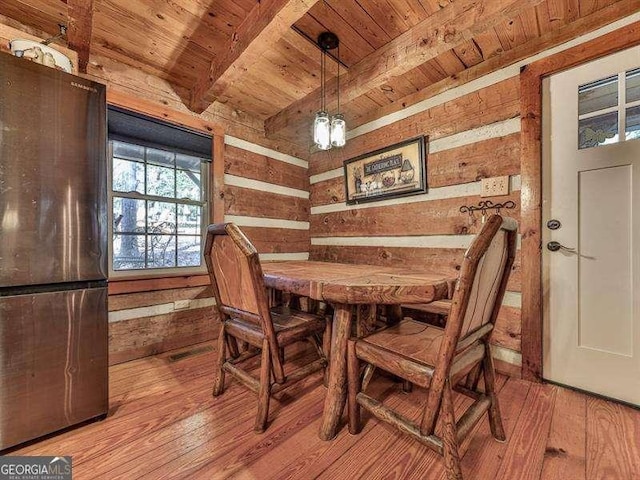 dining area featuring beamed ceiling, wooden walls, light hardwood / wood-style floors, and wooden ceiling