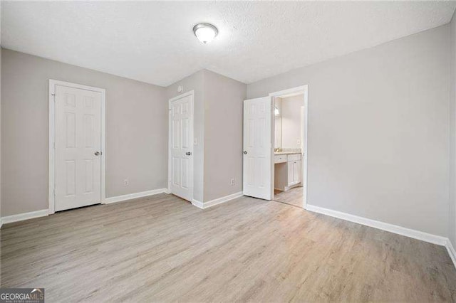 unfurnished bedroom featuring connected bathroom, a textured ceiling, and light wood-type flooring