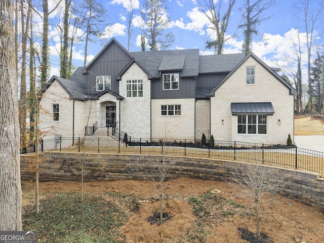 view of front facade with brick siding, a fenced front yard, board and batten siding, and roof with shingles