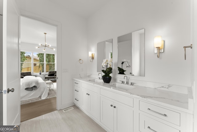 ensuite bathroom featuring an inviting chandelier, connected bathroom, a sink, and double vanity