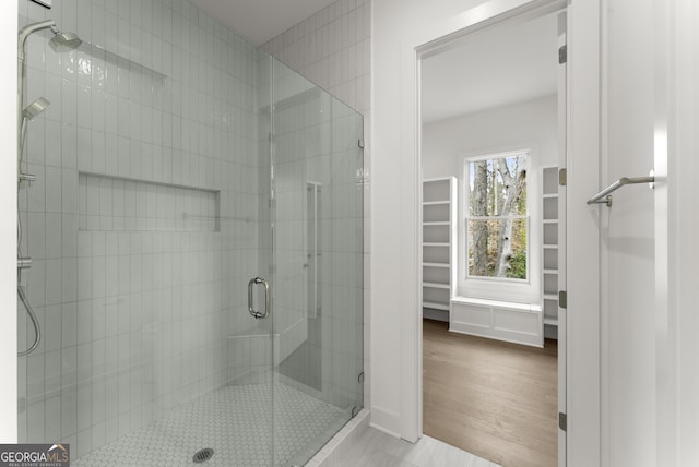 full bathroom with a spacious closet, a shower stall, and wood finished floors