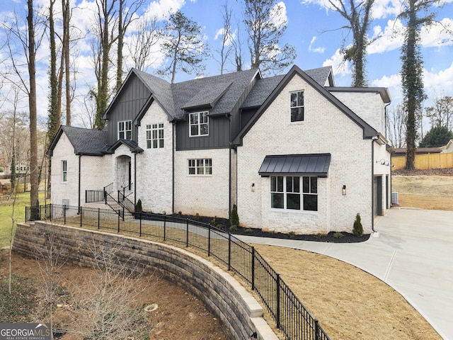 view of front of property with driveway, a shingled roof, fence, board and batten siding, and brick siding