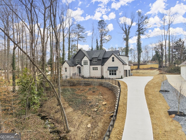 french country home featuring stone siding, fence, concrete driveway, and roof with shingles