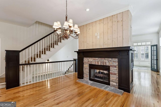 living room featuring crown molding, a stone fireplace, hardwood / wood-style floors, and a notable chandelier