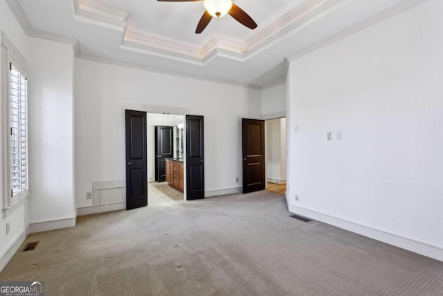 unfurnished bedroom with a towering ceiling, light colored carpet, ceiling fan, a tray ceiling, and crown molding