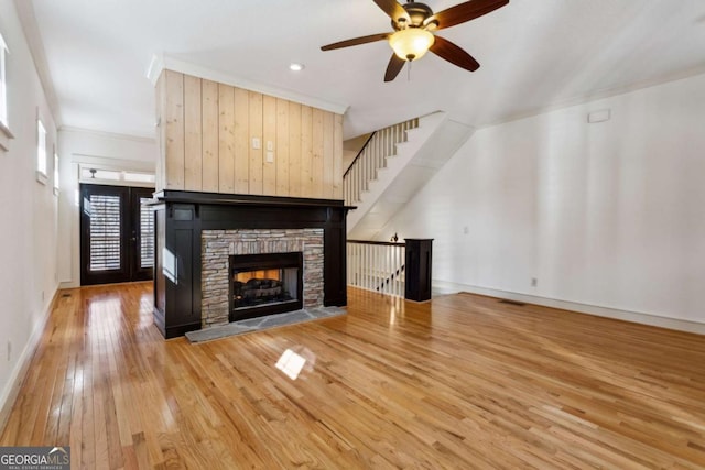 unfurnished living room featuring hardwood / wood-style flooring, ceiling fan, a stone fireplace, and crown molding