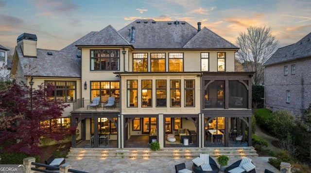 back house at dusk featuring a sunroom and a patio area