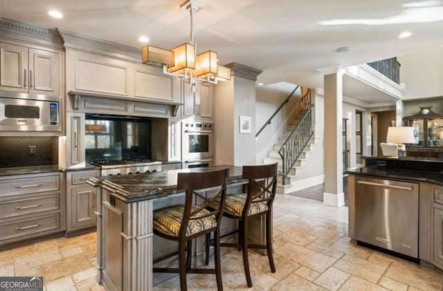 kitchen with pendant lighting, appliances with stainless steel finishes, dark stone countertops, a kitchen island, and a kitchen bar