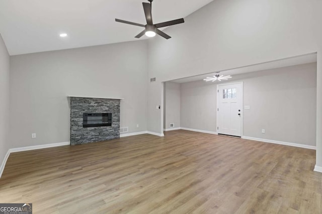 unfurnished living room with ceiling fan, a fireplace, high vaulted ceiling, and light wood-type flooring