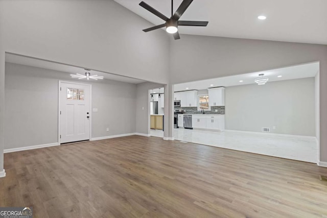 unfurnished living room with sink, high vaulted ceiling, light hardwood / wood-style floors, and ceiling fan