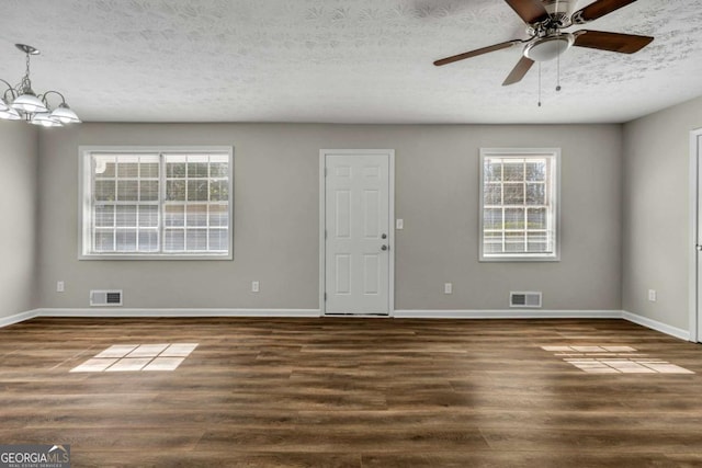 empty room with ceiling fan with notable chandelier, a wealth of natural light, a textured ceiling, and dark hardwood / wood-style flooring