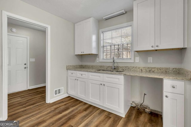 kitchen with sink, white cabinetry, dark hardwood / wood-style floors, built in desk, and light stone countertops