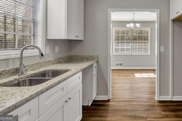 kitchen featuring sink, white cabinetry, light stone counters, a notable chandelier, and pendant lighting