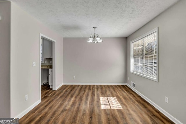 unfurnished room featuring an inviting chandelier, dark hardwood / wood-style flooring, and a textured ceiling