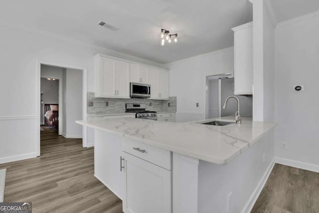 kitchen featuring white cabinetry, stainless steel appliances, kitchen peninsula, and light stone countertops