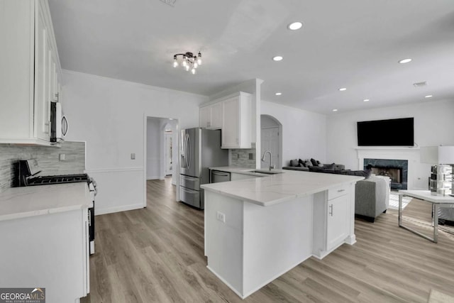 kitchen featuring appliances with stainless steel finishes, light stone counters, a fireplace, white cabinets, and kitchen peninsula